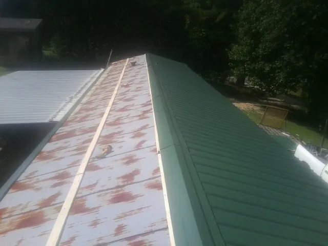 Old rusted panels beside newly installed green metal roofing — Wind Damage Roof Repair by Roofing Brothers in Rockville