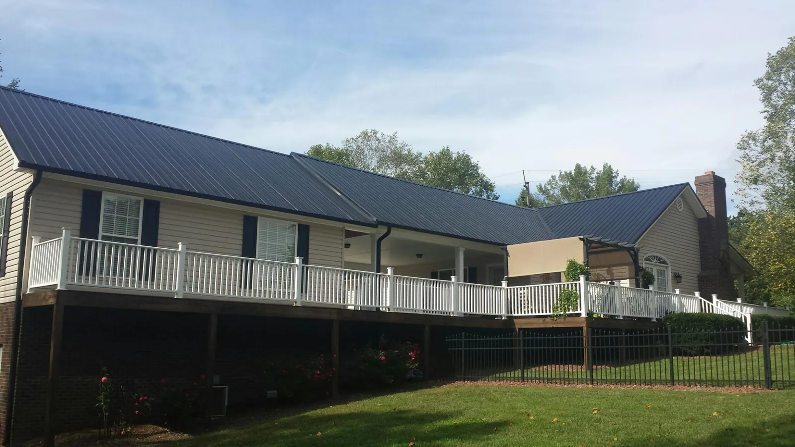 Black metal roof above a long white railed deck on a hillside home in Rockville